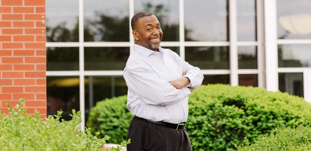 Candidate Antoine Jennings outdoors, smiling with his arms folded in front of a brick building.